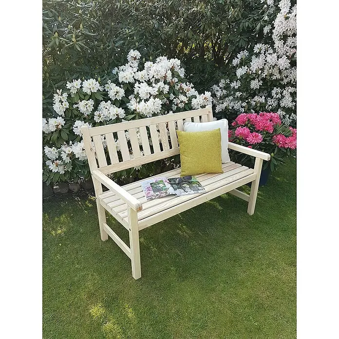 Promadino Gartenbank Johanna - B x T x H: 125 x 71 x 88,5 cm, Kiefer, Natur - Eine unbehandelte Holzgartenbank mit Kissen und einer Zeitschrift, eingebettet in üppige Blütenpracht. Ideal zum Entspannen im Garten.