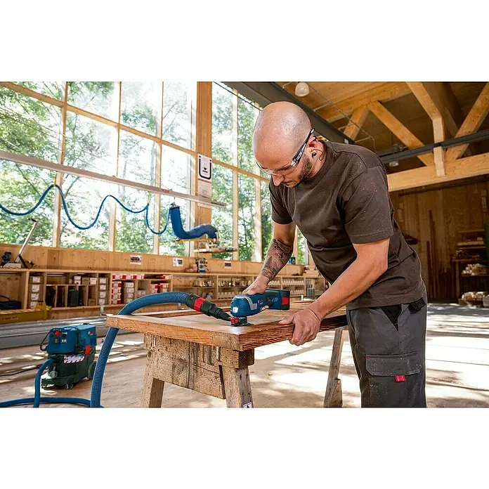 Bosch Professional AMPShare 18V Akku-Multifunktionswerkzeug GOP 18V-34 - 18 V, Ohne Akku - Mann arbeitet mit einem Bosch Multifunktionswerkzeug an einem Holzrahmen, mit Staubabsaugung. Für präzise Schleifarbeiten.