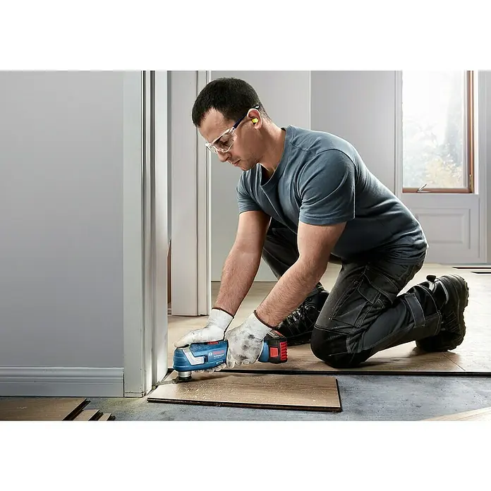 Bosch Professional AMPShare 18V Akku-Multitool GOP 18V-34 - 18 V, Ohne Akku - Mann arbeitet mit einem Bosch Multifunktionswerkzeug auf einem Holzboden, Schutzbrille und Handschuhe inklusive.