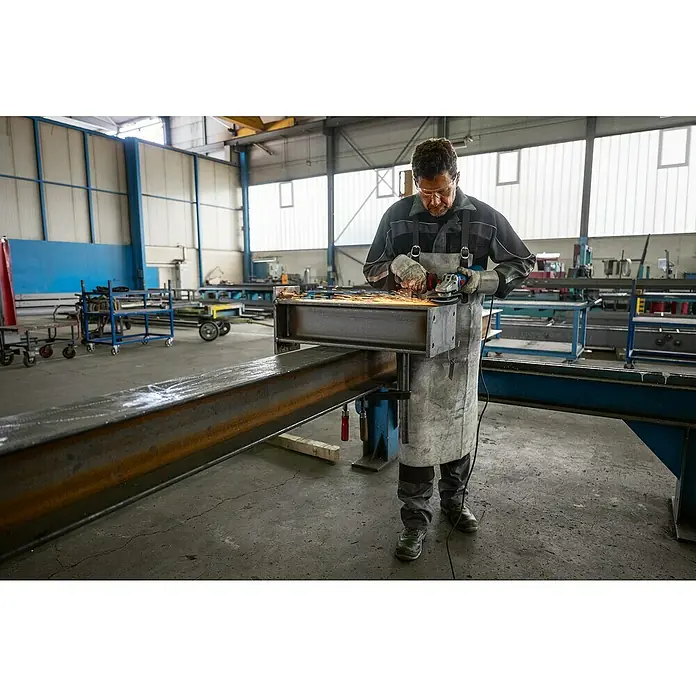 Bosch Professional Amoladora angular eléctrica PROFGWS12-125 - 1.200 W, Diámetro disco: 125 mm - Un trabajador con equipo de protección utiliza una amoladora angular sobre una pieza metálica en un taller, saltan chispas.