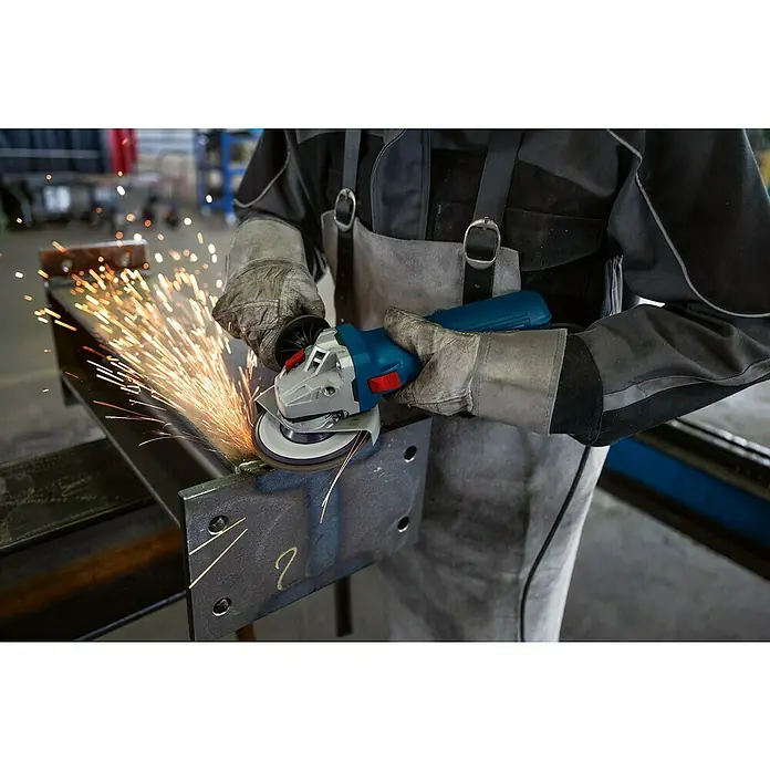 Bosch Professional Elektro-Winkelschleifer GWS 12-125 - 1.200 W, Durchmesser Scheibe: 125 mm - Metallarbeiter schleift Metall mit einem blauen Winkelschleifer, wobei Funken sprühen. Schutzkleidung ist unerlässlich.