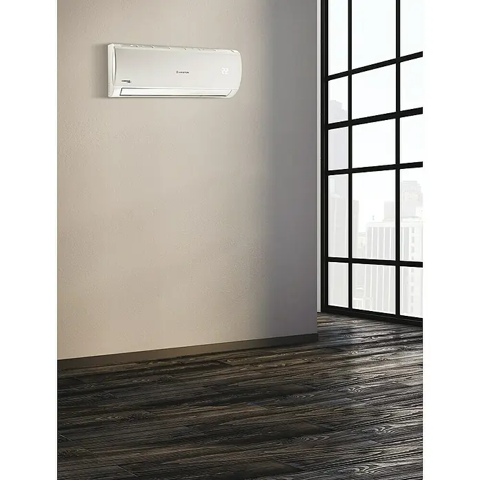 Ariston Aire acondicionado Inverter Alys R32 - 2.800 W, 2.600 W, 16 m², Blanco - Un aire acondicionado Ariston está montado en una pared en una habitación luminosa con pisos de madera oscura y una gran ventana con vista a una ciudad.