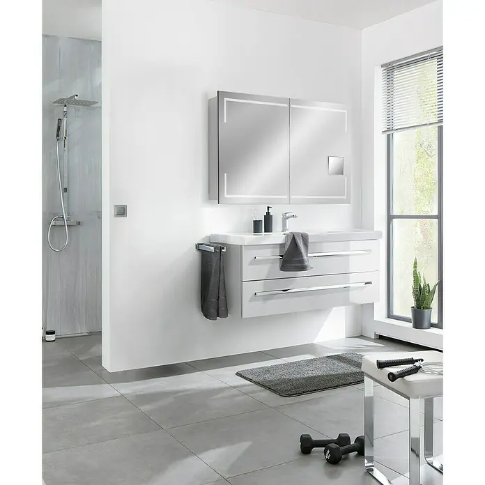 Lanzet K1 Badmöbel-Set K11W2 - 119,2 cm, Weiß - Das moderne Badezimmer präsentiert einen weißen Waschtisch mit passendem Spiegelschrank, akzentuiert durch schlichte, graue Textilien und Fitnessgeräte.