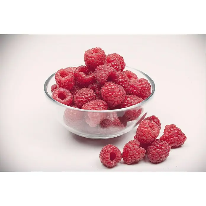 Piardino Himbeere Aroma Queen - Rubus idaeus 'Aroma Queen', Erntezeit: August - Frische Himbeeren in einer Glasschale und einige daneben. Die reifen Himbeeren sind saftig und verlockend.