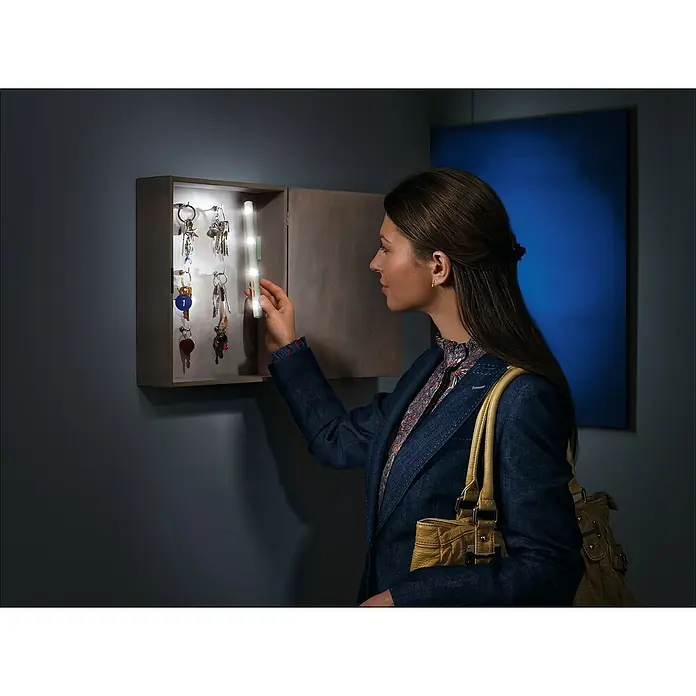 Ledvance Barra luminosa LED Lumistixx - Blanco diurno, Funciona con pilas, 1 ud. - Una mujer buscando una llave en un armario para llaves con una barra de luz LED integrada. ¡Práctico y elegante!
