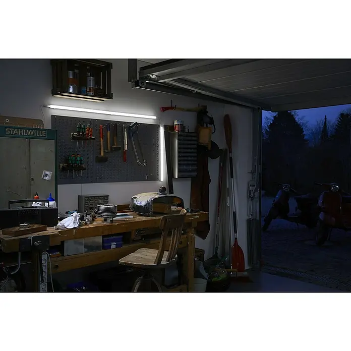 Osram LED-Lichtleiste Switch Batten - L x B x H: 31,3 x 2,2 x 3 cm, Lichtfarbe: Warmweiß, 4 W - Werkstatt-Interieur mit Werkbank und Werkzeugwand, beleuchtet durch eine helle LED-Leuchte. Im Hintergrund parken zwei Motorroller in der offenen Garage.