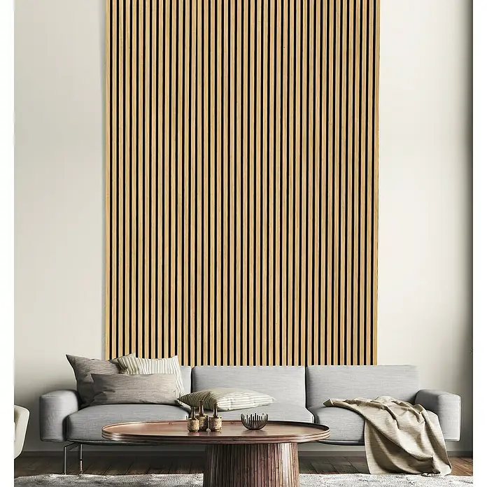 FN Neuhofer Akustikpaneel Acustico - Eiche natur, L x B x S: 1.195 x 572,5 x 19 mm - Das Bild zeigt eine moderne Lamellenwand aus Holz, die sich elegant über eine graue Couch erstreckt und dem Raum Struktur verleiht.