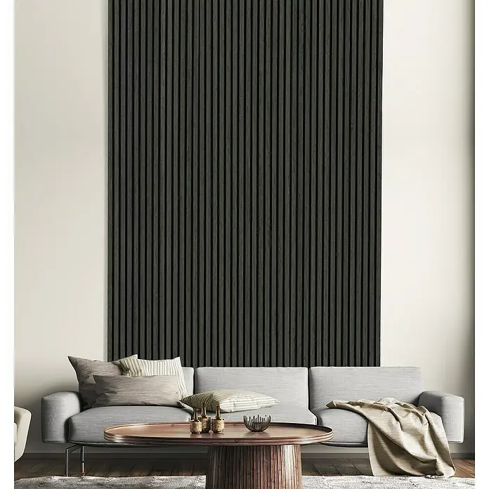FN Neuhofer Akustikpaneel Acustico - Dunkelgrau, L x B x S: 2.400 x 572,5 x 19 mm - Wohnzimmer mit einer Akustikplatte aus schwarzen Holzlatten an der Wand hinter einem grauen Sofa mit Kissen und einem runden Couchtisch.