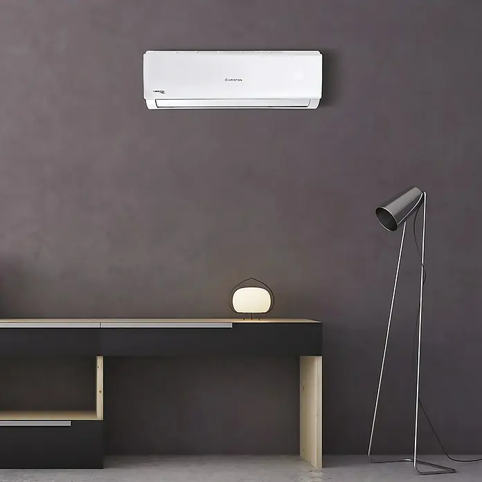 Ariston Aire acondicionado Inverter Alys R32 - 2.800 W, 2.600 W, 16 m², Blanco - Un aire acondicionado blanco Ariston está montado en una pared gris sobre una mesa moderna con lámparas, garantizando un clima interior confortable.