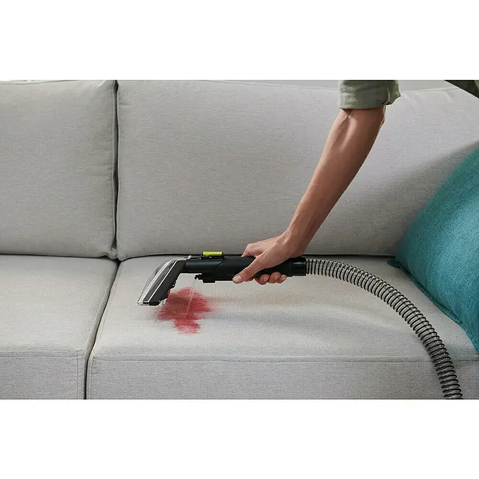 Ryobi ONE+ Akku-Waschsauger Pro RDC18BL-0 - 18 V, Ohne Akku, Behältervolumen: 1 l - Ein Handstaubsauger wird verwendet, um einen Fleck auf einem grauen Sofa zu entfernen. Ideal für die schnelle Reinigung von Polstern und Teppichen.