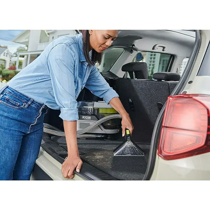 Ryobi ONE+ Akku-Waschsauger Pro RDC18BL-0 - 18 V, Ohne Akku, Behältervolumen: 1 l - Eine Frau reinigt den Kofferraum eines Autos mit einem RYOBI Akku-Spot-Reiniger. Das Gerät ist kompakt und tragbar.
