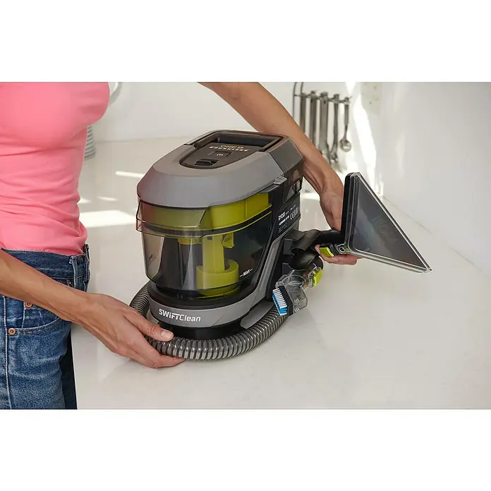 Ryobi ONE+ Akku-Waschsauger Pro RDC18BL-0 - 18 V, Ohne Akku, Behältervolumen: 1 l - Nahaufnahme einer Person, die einen tragbaren Ryobi SwiftClean Teppichreiniger mit Aufsatz auf einer weißen Oberfläche hält.