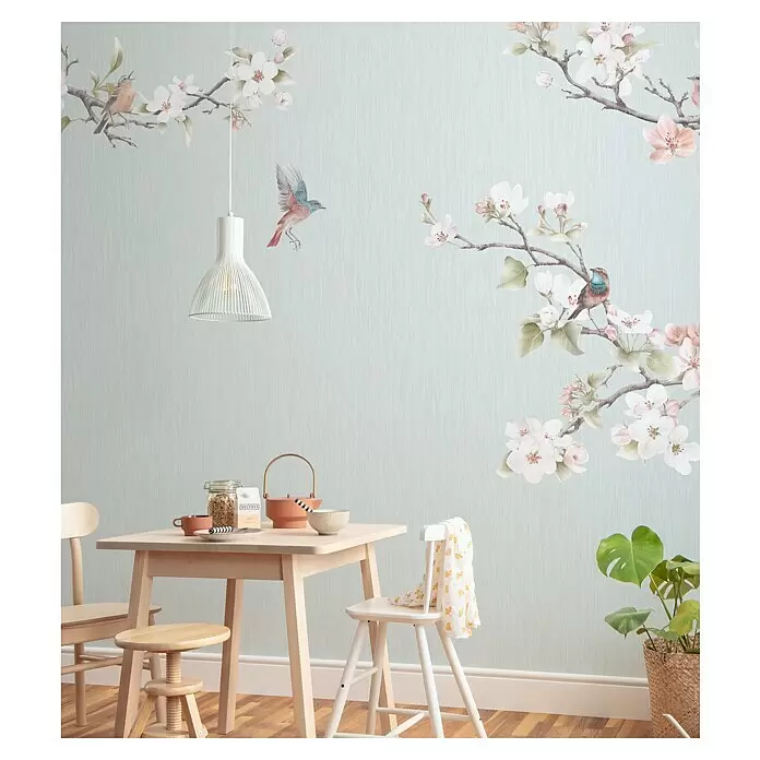 Komar Pure 2 Fototapete Apple Blossom - B x H: 300 x 250 cm, Vlies - Leichter Holztisch mit passenden Stühlen und einer weißen Pendelleuchte in einem Raum mit Vogel- und Blüten-Tapete.