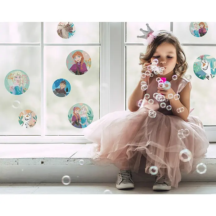 Komar Fenstersticker Frozen Royal Bubbles - 30 x 30 cm - Ein Mädchen im rosa Kleid sitzt am Fenster, umgeben von Frozen-Aufklebern, und pustet Seifenblasen. Niedliche Dekoration für Kinderzimmer.