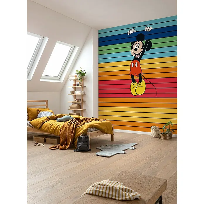 Komar Fototapete Disney Mickey Magic Rainbow - B x H: 300 x 250 cm, Vlies - Kinderzimmer mit farbenfroher Mickey Mouse Wandtapete, Holzfußboden und gemütlichem Bett mit gelber Bettwäsche.