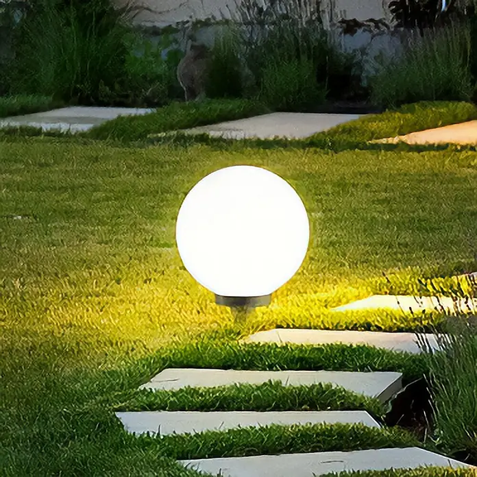 Starlux Kugel-Außenleuchte Kira - 30 cm, Weiß - Eine leuchtende Kugel-Gartenleuchte erhellt einen grünen Rasenweg mit Steinplatten. Schafft eine warme und einladende Atmosphäre im Garten.