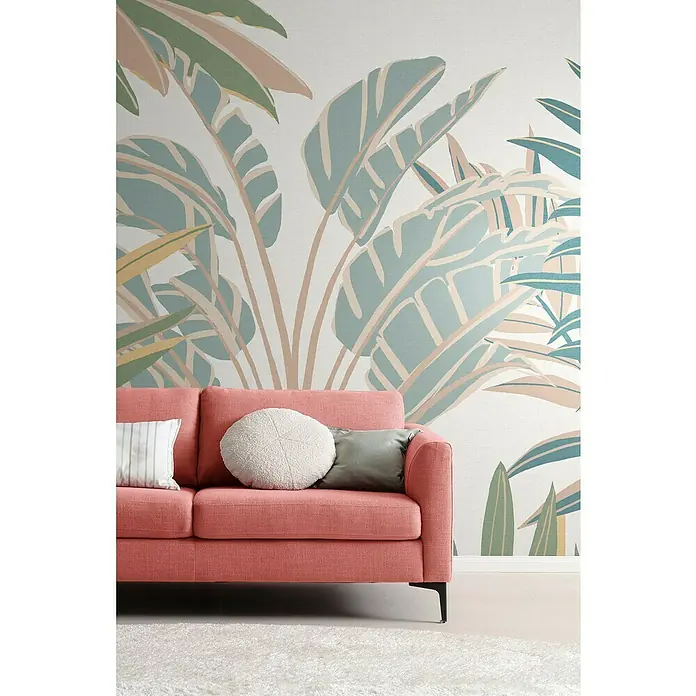 SCHÖNER WOHNEN-Kollektion Cosyliving Fototapete Dschungel - B x H: 318 x 300 cm, Vlies, Weiß-Mehrfarbig - Ein modernes, korallfarbenes Sofa mit Zierkissen vor einer tropischen Tapete. Das Sofa hat schlanke, schwarze Beine.
