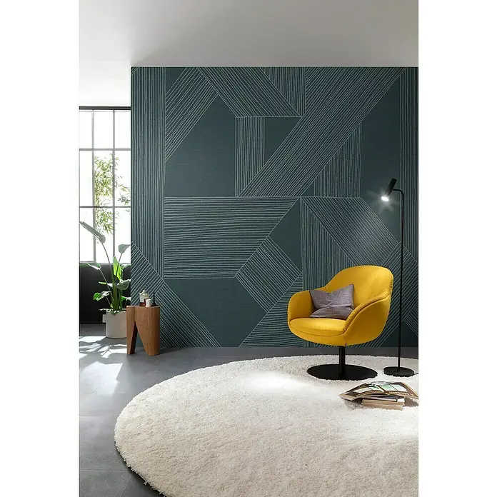 SCHÖNER WOHNEN-Kollektion Cosyliving Fototapete Linien - B x H: 265 x 300 cm, Vlies, Petrol-Hellgrau - Gelber Sessel auf rundem Teppich vor einer Wand mit geometrischem Muster. Die Lampe rechts spendet Licht und Bücher liegen auf dem Teppich.