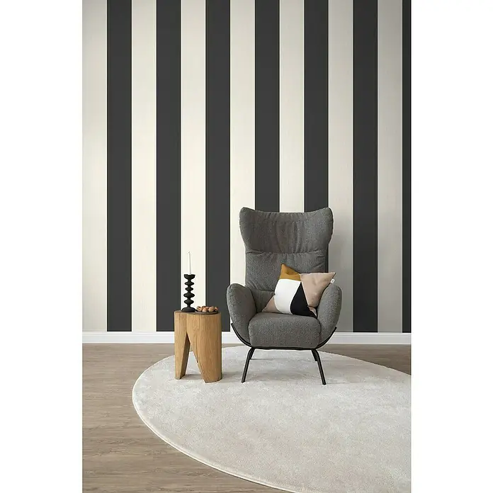 SCHÖNER WOHNEN-Kollektion Cosyliving Fototapete Streifen - B x H: 212 x 300 cm, Vlies, Schwarz-Weiß - Einrichtungsidee mit einem grauen Sessel mit Kissen auf einem Teppich vor einer gestreiften Wand.