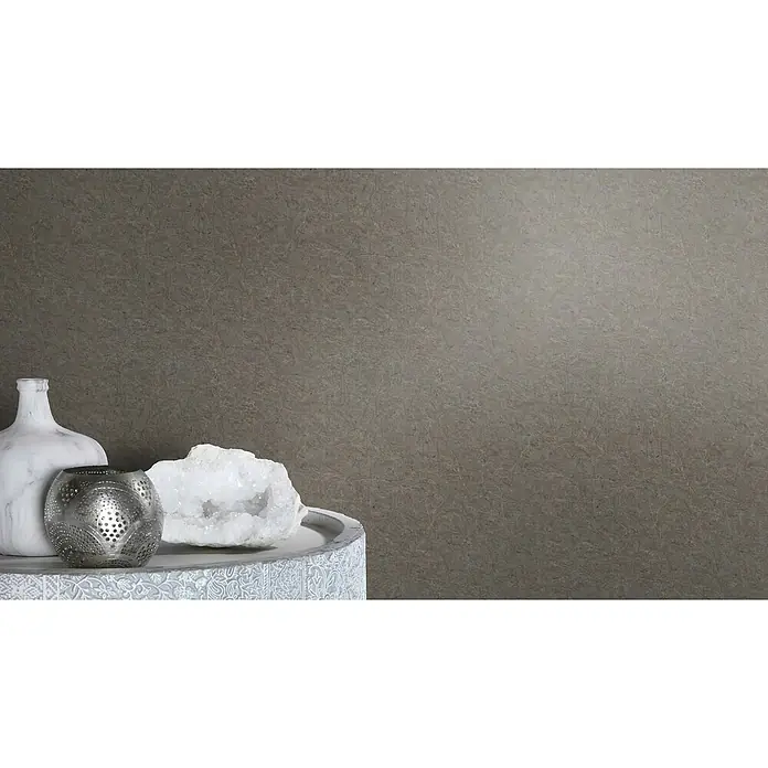 SCHÖNER WOHNEN-Kollektion Cosyliving Vliestapete MARBLE Marmor - Anthrazit, Steinoptik, 10,05 x 0,53 m - Eine Nahaufnahme eines Arrangements mit einer Marmorvase, einer Metalllaterne und einem Quarzkristall auf einem dekorativen Sockel vor einem grauen Hintergrund.