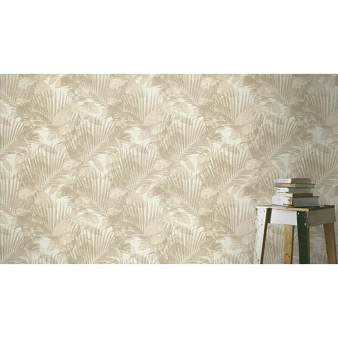SCHÖNER WOHNEN-Kollektion Cosyliving Vliestapete TROPICAL Schattenblatt - Sand, Floral, 10,05 x 0,53 m - Nahaufnahme einer Wand mit beigem Palmenblatt-Tapetenmuster und einem kleinen Tisch mit Büchern, der den botanischen Look verstärkt.