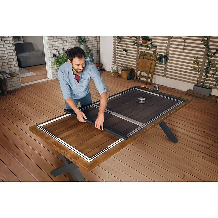 Tesa Puerta con protección contra insectos Falt - Antracita, Montaje de la mosquitera: Pinzas - Un hombre monta un marco de pantalla en una mesa, diseñado para evitar que entren insectos y proteger la casa de las plagas.