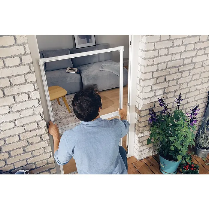 Tesa Puerta con protección contra insectos Falt - Antracita, Montaje de la mosquitera: Pinzas - Un hombre instala un marco de pantalla para insectos en una puerta para proteger la casa de los insectos.
