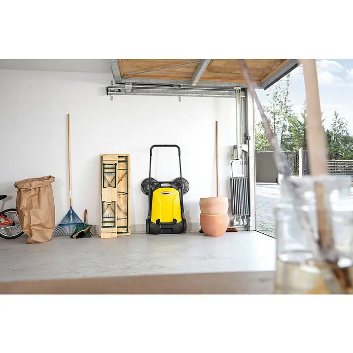 Kärcher Handkehrmaschine S 4 Twin - Flächenleistung: 2.400 m²/h, 20 l - Der gelbe Kärcher Kehrmaschine in einer Garage, umgeben von Gartenwerkzeugen, bietet eine effiziente Lösung für die Reinigung.