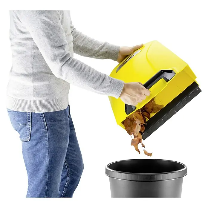 Kärcher Handkehrmaschine S 4 - Flächenleistung: 1.800 m²/h, 20 l - Eine Person entleert einen Kärcher Kehrmaschinebehälter mit Laub in einen Mülleimer. Praktisch für die Gartenarbeit!