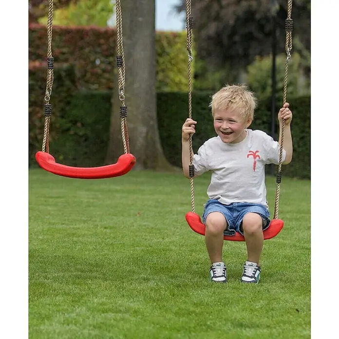Swing King Doppelschaukel Ava - L x B x H: 73 x 245 x 170 cm, Holz, Blau - Fröhlicher Junge schwingt auf roter Schaukel im Garten, umgeben von Grün. Ein zweites, leeres Schaukelbrett ist daneben sichtbar.