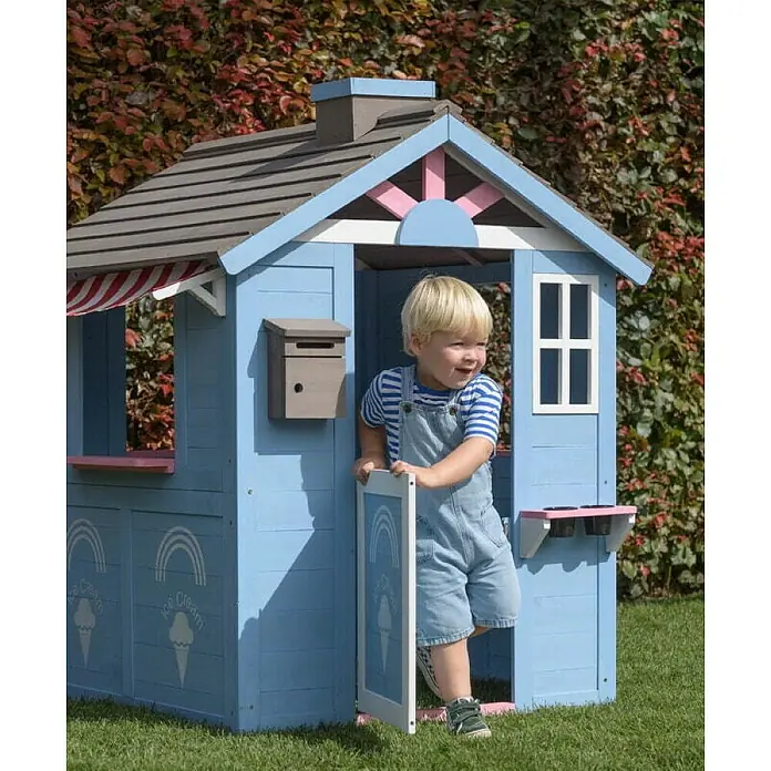Swing King Spielhaus Icecream - L x B x H: 120 x 108 x 135 cm, Holz, Blau/Weiß/Rosa/Grau - Ein Junge spielt im strahlend blauen KidKraft Spielhaus mit Eisdielen-Motiv, das über ein Fenster und eine Markise verfügt.
