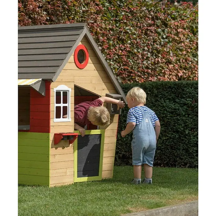 Swing King Spielhaus Fairytale - L x B x H: 140 x 106 x 145 cm, Holz, Gelb/Rot/Weiß/Holz/Grau - Zwei Kinder spielen in einem bunten Holzspielhaus im Garten. Das Spielhaus hat ein Fenster, eine Tür und ein markantes rotes Detail.