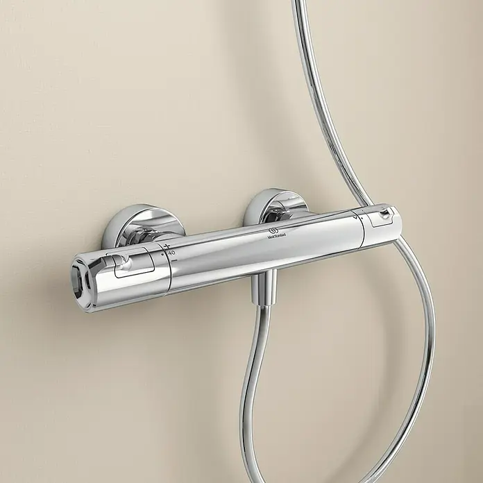Ideal Standard Ceratherm Brausethermostat T50 - Chrom - Nahaufnahme einer glänzenden Ideal Standard Duscharmatur an einer beigen Wand. Der Chrom-Thermostat ist mit Temperaturanzeigen versehen.