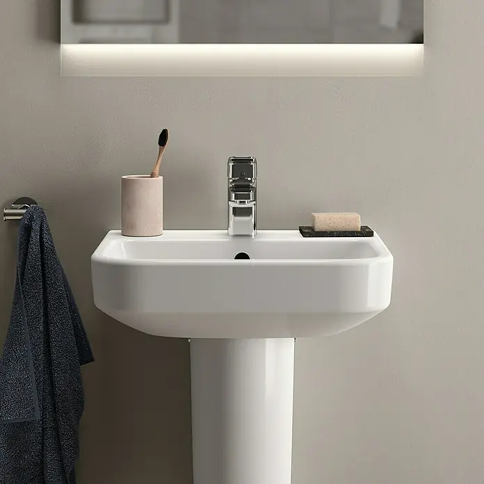 Ideal Standard i.life B WaschbeckenB x L: 45 x 38 cm, Ohne Spezialglasur, Hahnloch: Mitte, Mit Überlauf, Weiß - Ein stilvolles, modernes Waschbecken mit Armatur, Seife und Handtuch in einem hellen Badezimmer.