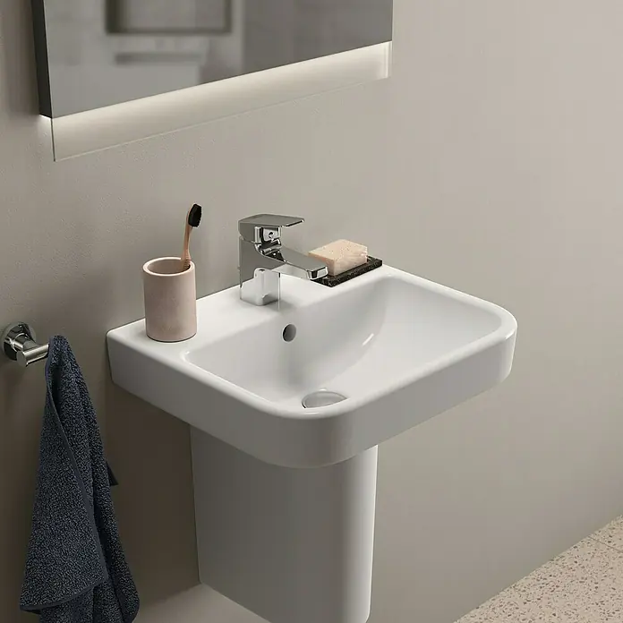 Ideal Standard i.life B Waschbecken - B x L: 45 x 38 cm, Ohne Spezialglasur, Hahnloch: Mitte, Mit Überlauf, Weiß - Nahaufnahme eines modernen Waschbeckens mit Armatur, Seife, Zahnbürste und Handtuch in einem stilvollen Badezimmer.