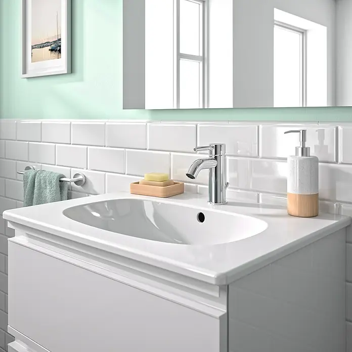 Ideal Standard Ceraline Waschtischarmatur - Chrom, Glänzend, Mit Ablaufgarnitur - Modernes Badezimmerwaschbecken mit stilvoller Armatur, Seifenspender und Handtuchhalter vor hellgrünem Hintergrund.