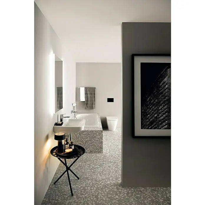 Ideal Standard i.life B Waschbecken - B x L: 45 x 38 cm, Ohne Spezialglasur, Hahnloch: Mitte, Mit Überlauf, Weiß - Badezimmer mit Waschbecken, Badewanne und Toilette, stilvoll eingerichtet mit Terrazzoboden und dunklem Beistelltisch, beleuchtetem Spiegel und einem Kunstwerk.