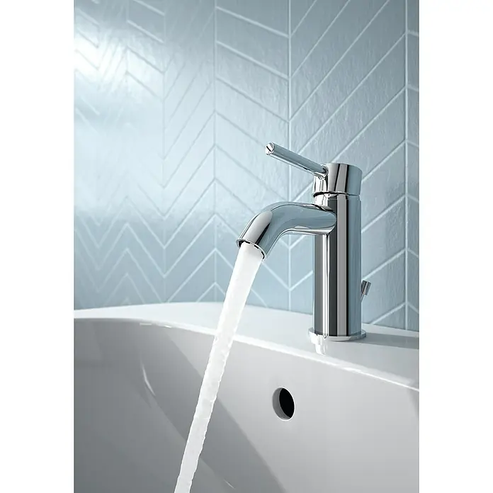 Ideal Standard Ceraline Waschtischarmatur - Chrom, Glänzend, Mit Ablaufgarnitur - Nahaufnahme einer modernen Chromarmatur, aus der Wasser in ein weißes Waschbecken fließt, vor einem Hintergrund mit blauen Fischgrätenfliesen.