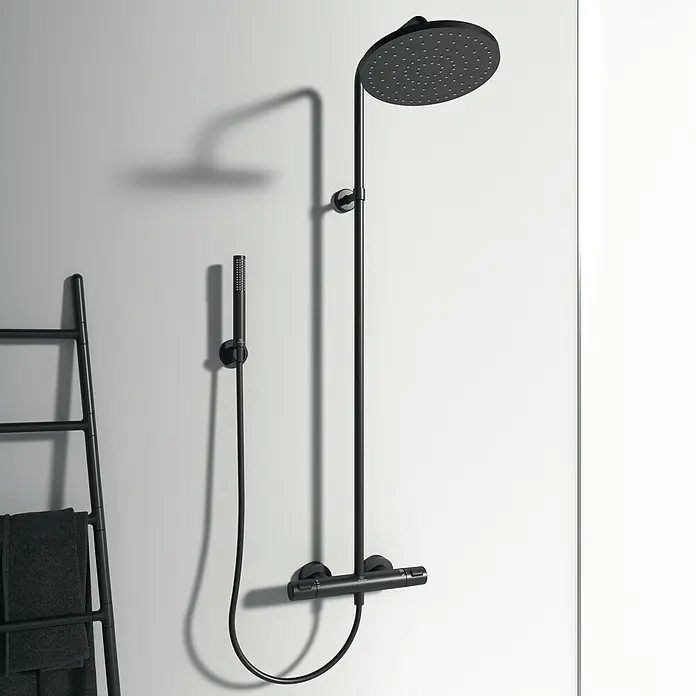 Ideal Standard Ceratherm Duschsystem T25 - Mit Thermostatarmatur, Lochabstand: 70 cm, Anzahl Strahlarten: 1 Stk., Schwarz - Schwarze Duschgarnitur mit rundem Duschkopf, Handbrause und Thermostatmischer an einer hellen Badezimmerwand.