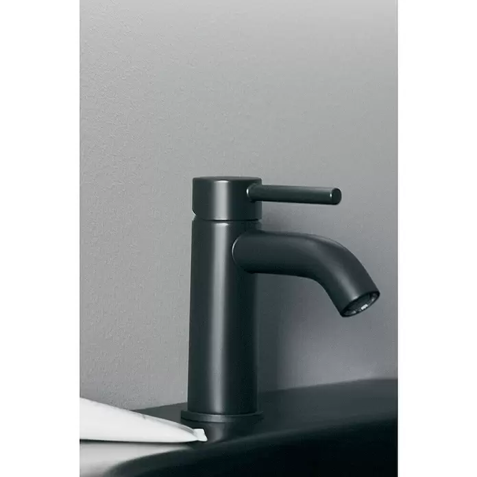 Ideal Standard Ceraline Grifo de lavabo - Cromo, Mate, Con juego de desagüe «Push-Open» - Grifo moderno negro mate montado en un fregadero oscuro, con una manija de palanca única. Un tubo blanco está abajo a la izquierda.