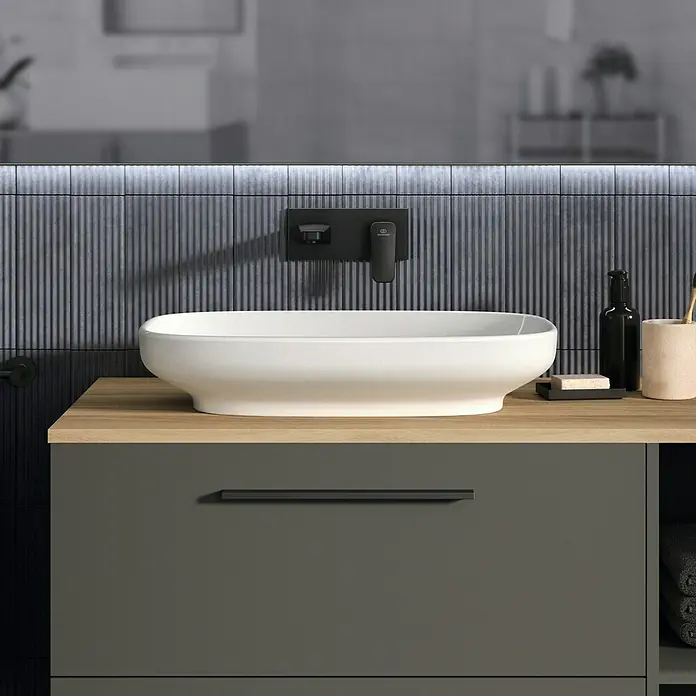 Ideal Standard Ceraplan WaschtischarmaturSchwarz, Matt - Das Bild zeigt ein modernes Badezimmerwaschbecken in Weiß mit Armatur vor einer stilvollen, gefliesten Wand und einem Waschtischunterschrank.