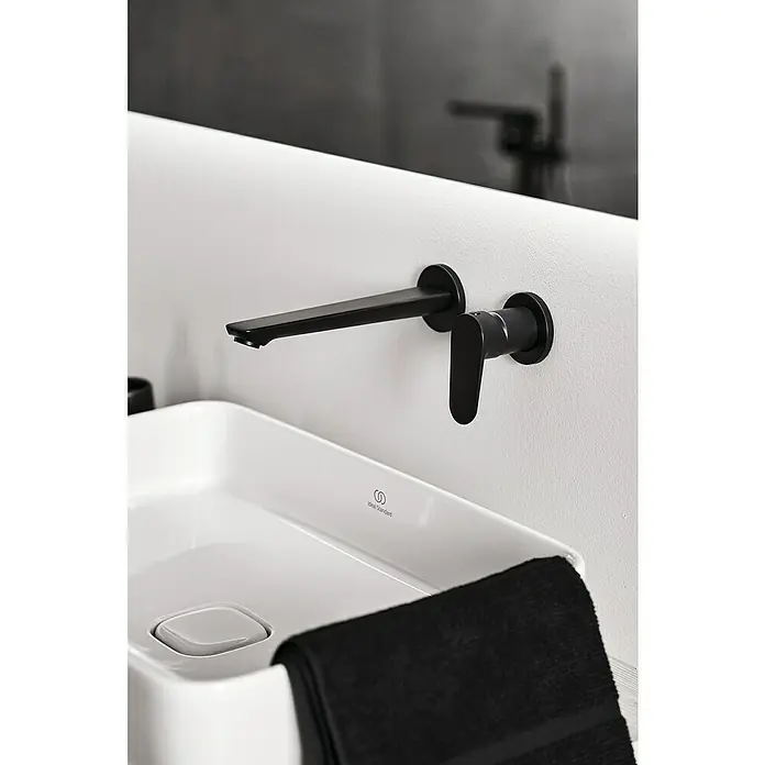 Ideal Standard Cerafine O Waschtischarmatur - Schwarz, Matt - Schwarzer Wandmontierter Wasserhahn über einem weißen Waschbecken mit einem schwarzen Handtuch.