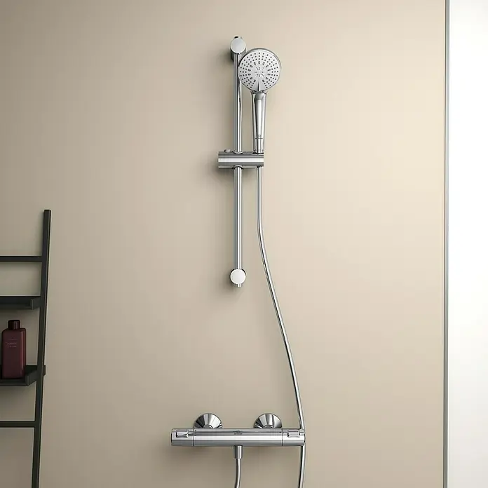 Ideal Standard Ceratherm Brausethermostat T25Chrom, Glänzend - Nahaufnahme einer glänzenden, verchromten Duschgarnitur an einer beigen Wand, die modernes Design und Funktionalität vereint.