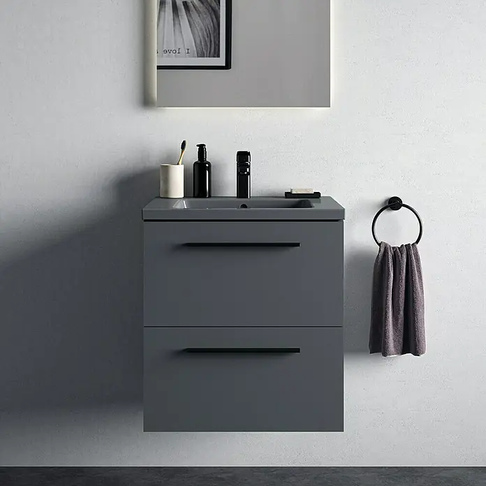Ideal Standard Ceraplan Waschtischarmatur H90 - Schwarz, Matt, Mit Ablaufgarnitur - Grauer Badezimmerschrank mit zwei Schubladen, einer Armatur, einem Spiegel und einem Handtuchring an einer grauen Wand.