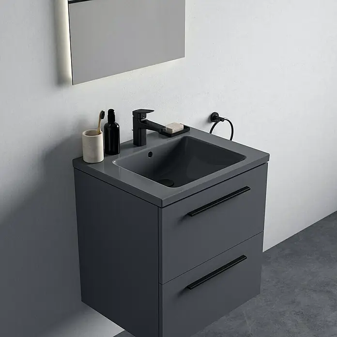 Ideal Standard Ceraplan Waschtischarmatur H90 - Schwarz, Matt, Mit Ablaufgarnitur - Graues Badezimmerwaschbecken mit zwei Schubladen, schwarzer Armatur, Seife, Zahnbürste und Handtuchring an einer weißen Wand.
