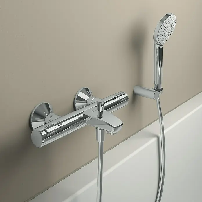 Ideal Standard Ceratherm Wannenthermostat T25Chrom, Glänzend - Nahaufnahme eines modernen Chrom-Duschsets mit Handbrause und Armatur an einer beige Wand.