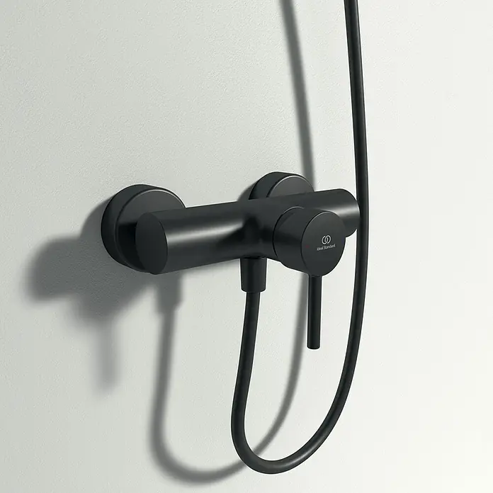 Ideal Standard Ceraline Brausearmatur - Schwarz, Matt - Schwarze Duscharmatur von Ideal Standard, montiert an einer weißen Wand, mit Schlauch und Bedienelementen für die Dusche.
