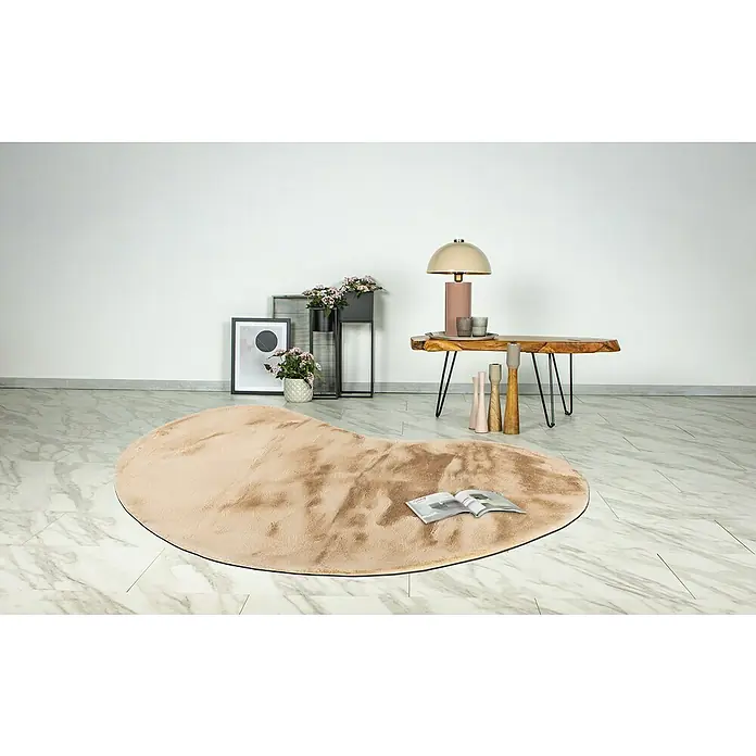 Fellteppich Happy - Beige, 230 x 160 cm, Oval, 100 % Polyester (Flor) - Ein beigefarbener, herzförmiger Teppich liegt auf einem Marmorboden, mit einem Buch darauf, für eine warme und stilvolle Atmosphäre.