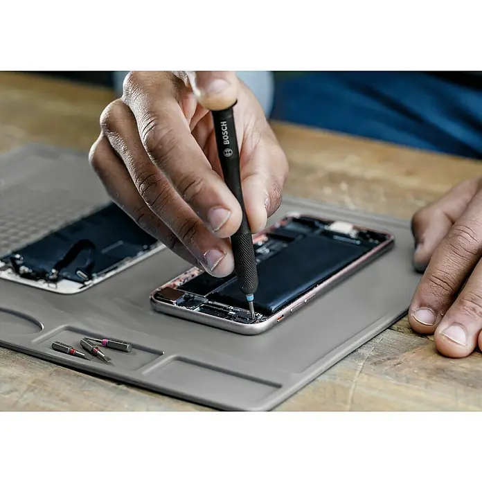 Bosch Bit-Set Precision - 42 -tlg. - Ein Techniker, der ein Smartphone mit einem Bosch-Präzisionsschraubendreher auf einer Arbeitsmatte repariert.