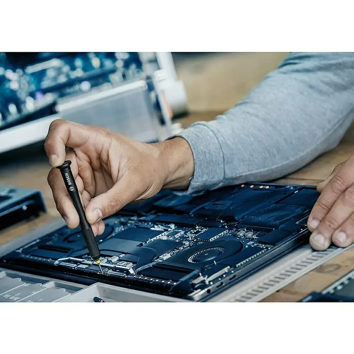 Bosch Bit-Set Precision - 42 -tlg. - Ein Detailaufnahme eines Bosch-Schraubendrehers in Aktion, der einen Laptop repariert, Fokus auf Präzision und Technik.